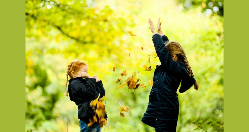 Two little girls playing in the autumn leaves